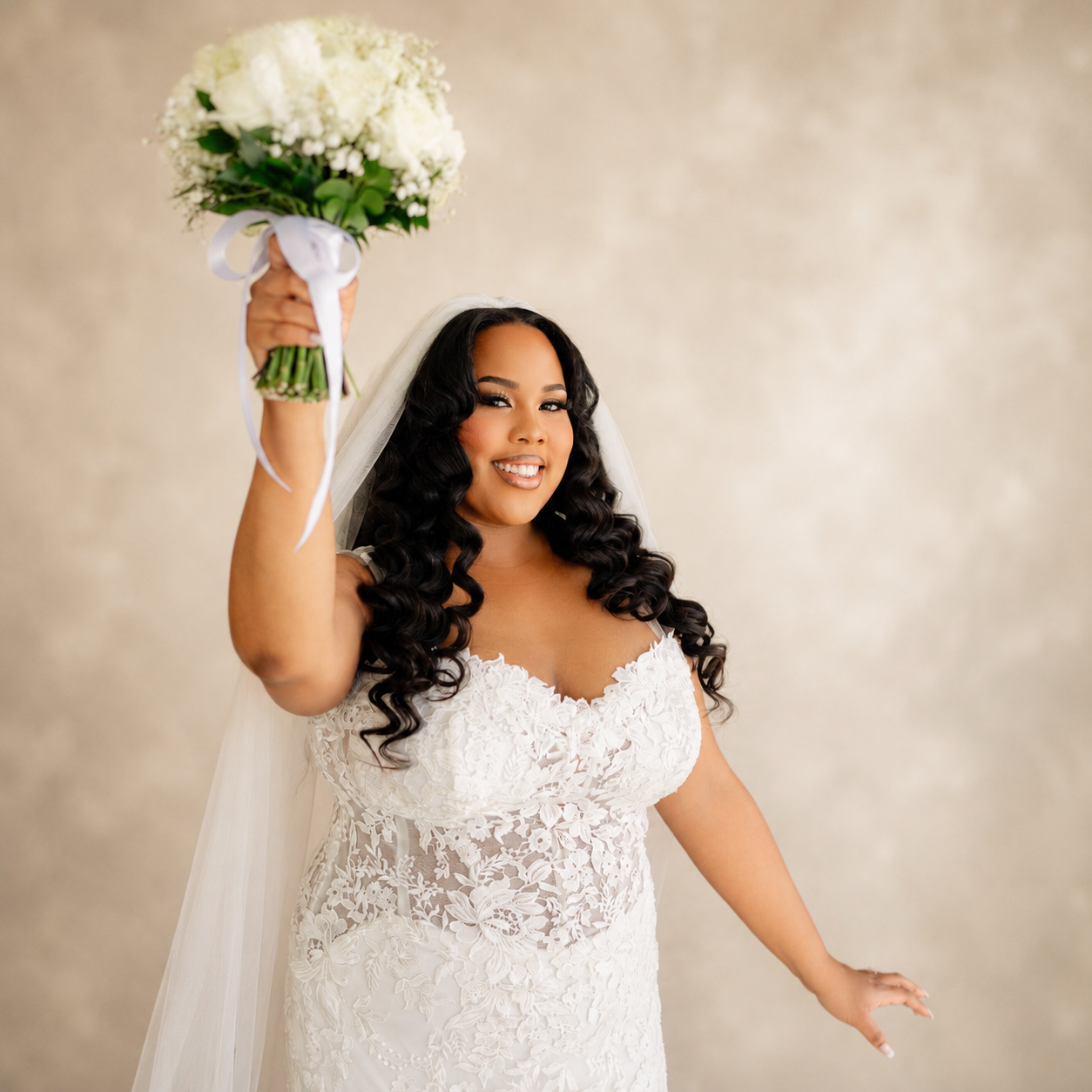 Bride in lace gown and veil holding bouquet high with long bouncy curls